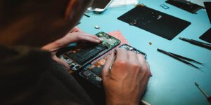 Technician repairing an opened smartphone on a workbench with repair tools and phone parts nearby.
