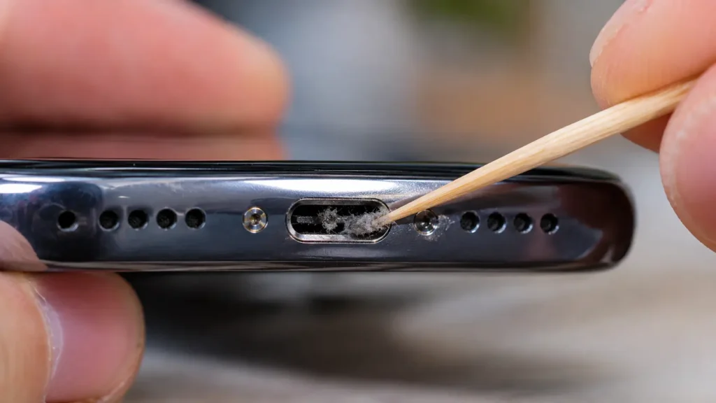 Person using a wooden toothpick to gently clean lint from a phone's charging port